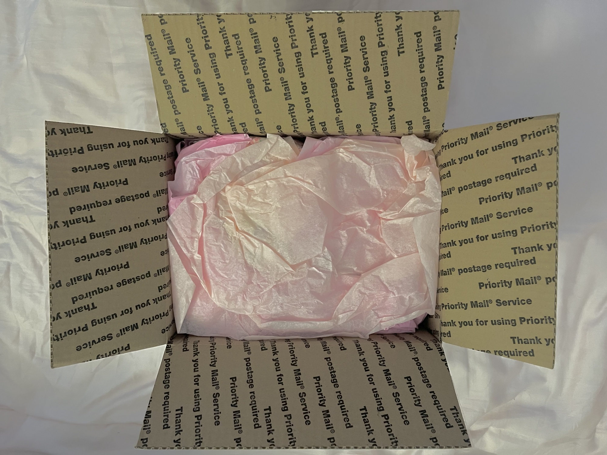 A photograph of the Priority Mail box now open, showing a bunch of pink tissue paper in the center.